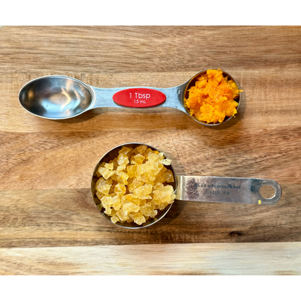 1 tablespoon of orange zest and 1/4 cup of chopped crystalized gingers on wooden cutting board.