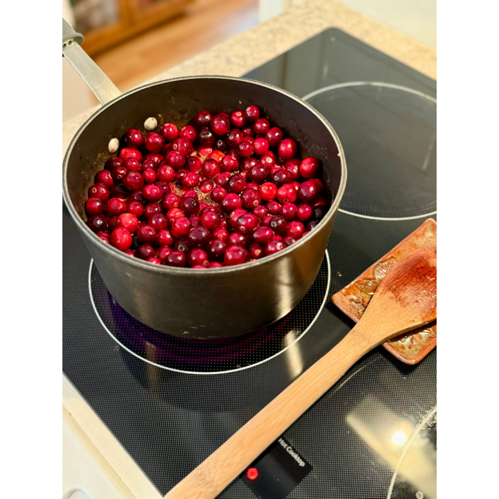 Image of cranberries o a stove stop cooking in a medium saucepan with wooden spoon