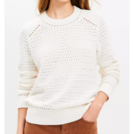 Woman in white pointelle sweater with rust jeans.