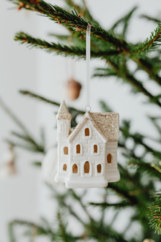 Image of white Christmas village house ornament with sparkly roof hanging from the Christmas tree.