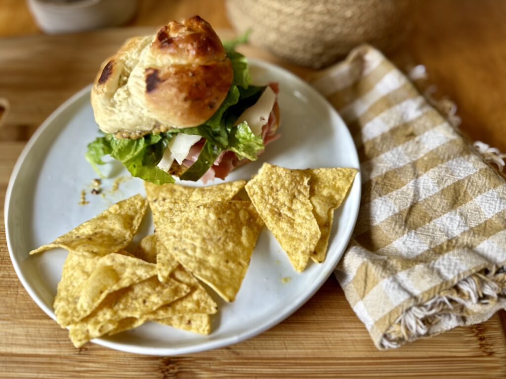 Image of leftover roll on white plate with chips next to a beige gingham cloth napkin.