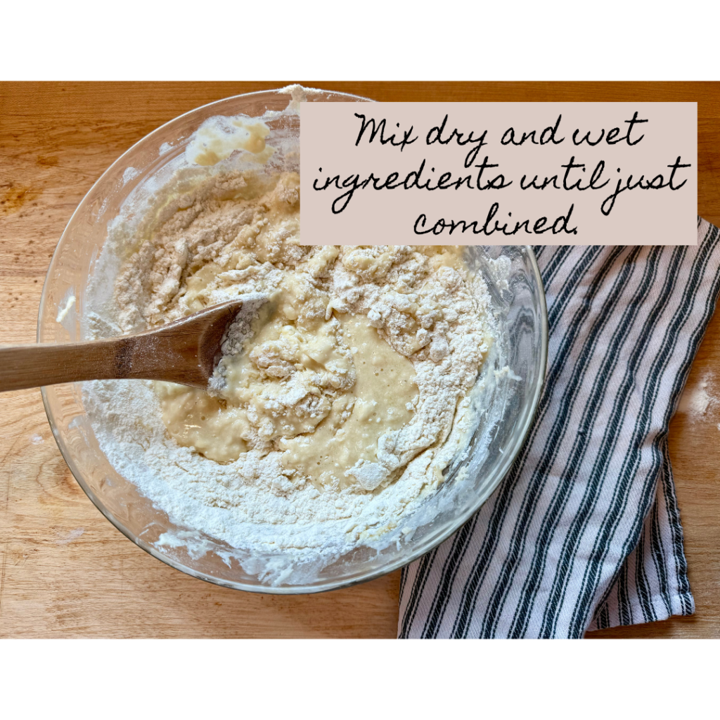 Image of wet and dry ingredients combined in medium glass bowl with wooden spoon. Items are on a wooden cutting board next to a black and white stripped cloth napkin. Text says "mix dry and wet ingredients until just combined."