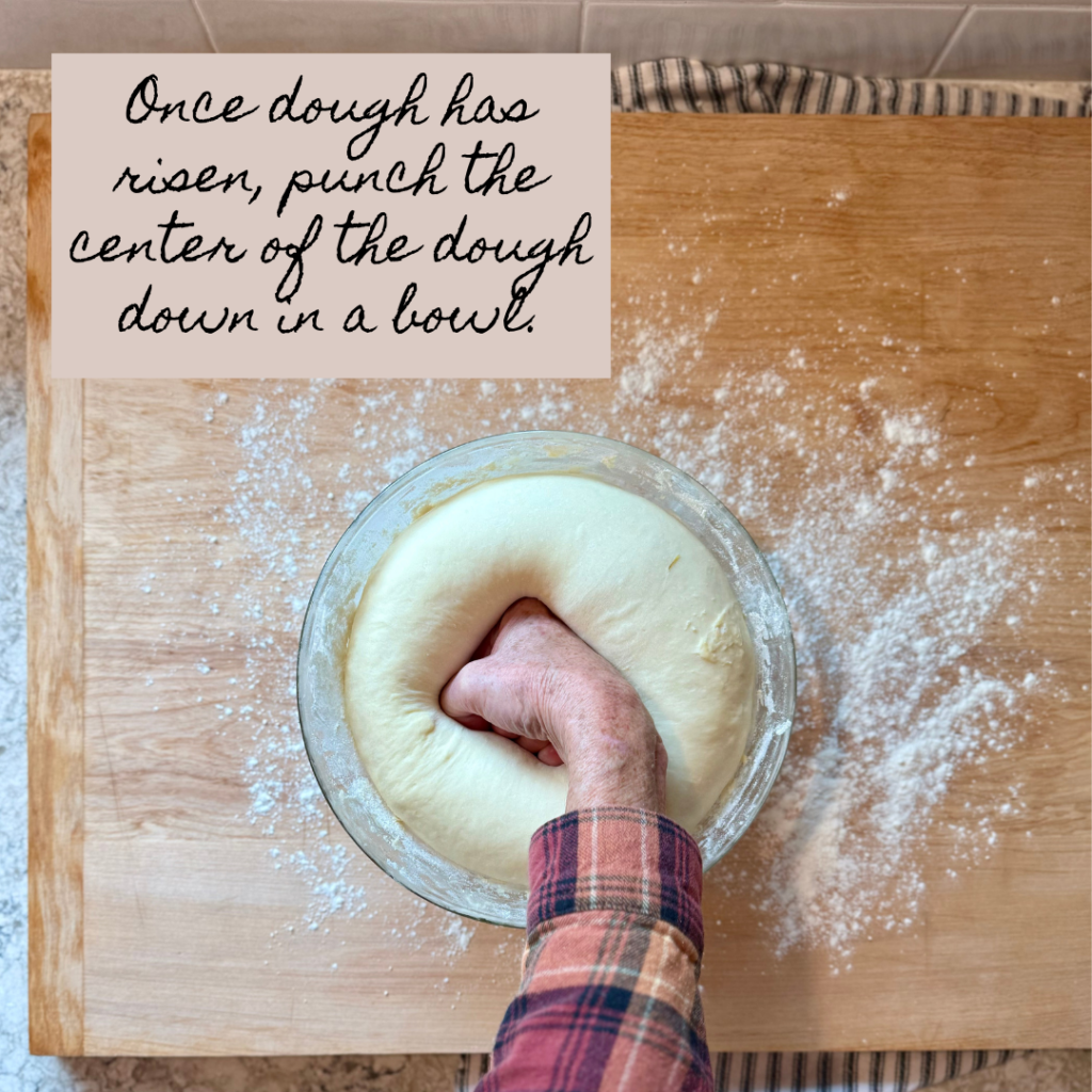 Image of woman punching dough in center after it has risen. Dough is in glass bowl on a lightly floured wooden surface.