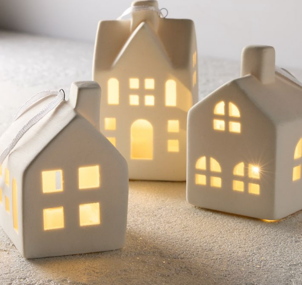 Image of 3 white Christmas village houses ornaments. Houses are two stories with chimneys and windows that are lit up. 