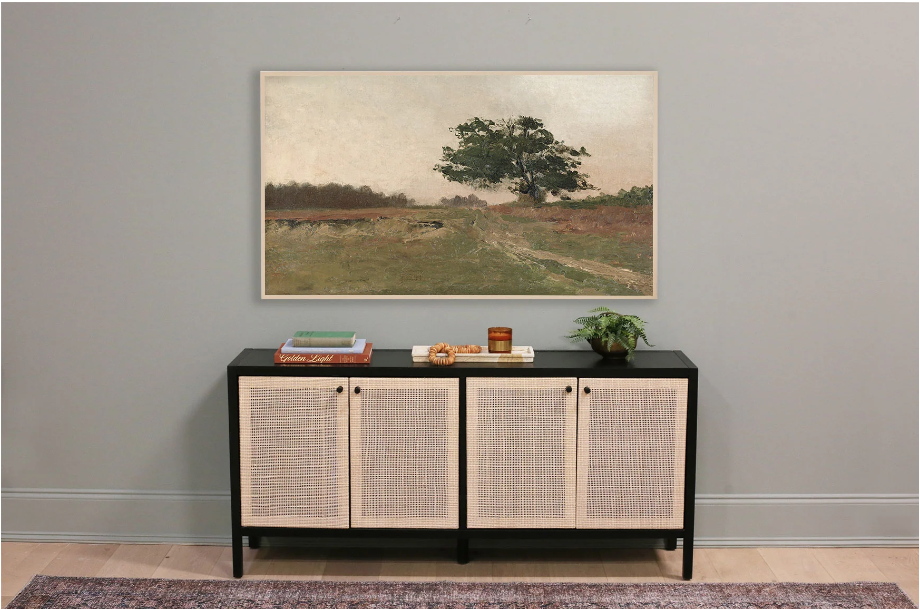 samsung frame tv art. Image of landscape of oak tree in front of green field on grey-green wall over black and tan credenza with red  vintage rug in front. 