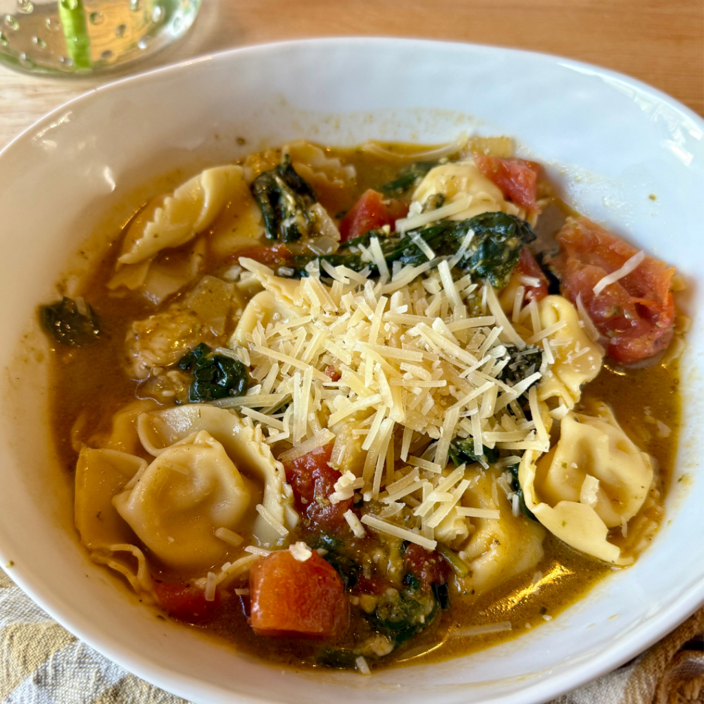 easy tortellini recipes. Image of white bowl of tortellini soup with spinach, tomatoes, and topped with parmesan.