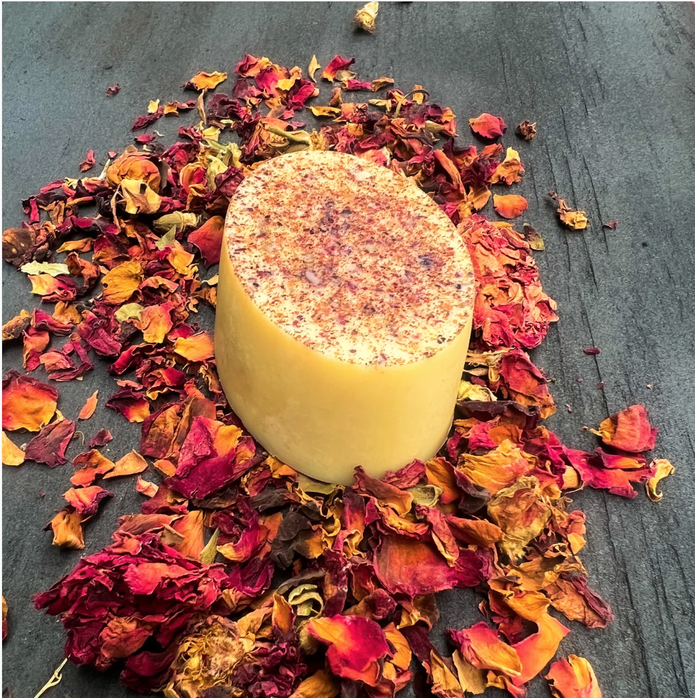 best clean skincare brands. Image of yellow lotion bar (looks like a bar of soap) that is surrounded by dried orange, yellow, and red flowers on a grey wooden table.