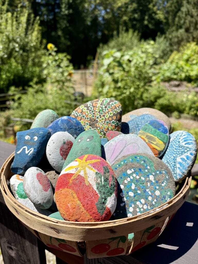 art project for kids. Image of basket of painted rocks in front a garden.