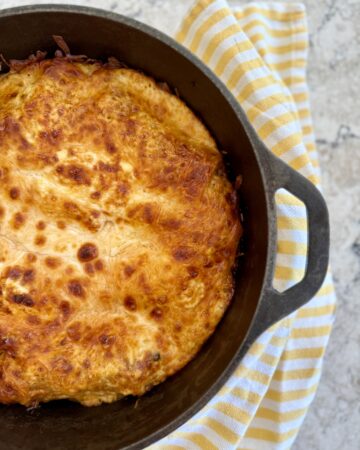 dutch oven lasagna. Picture of lasagna in cast iron dutch oven on grey quartz countertop with yellow and white striped cloth napkin.