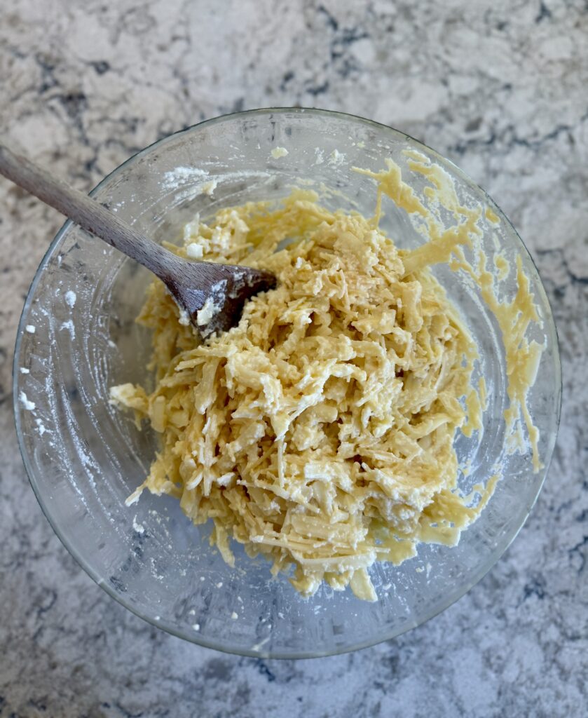 easy dutch oven lasagna. Image of mixture of egg, ricotta, mozzarella, and parmesan in a glass bowl on a grey and white quartz countertop. 