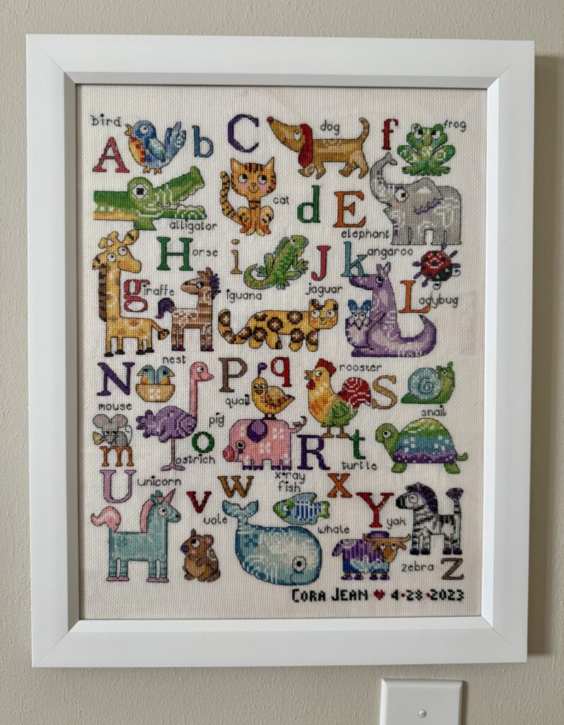 Close up of framed cross stitching with colorful alphabet and animals.