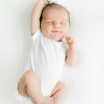 baby registry list. Image of newborn baby in white onesie stretching arm over head.