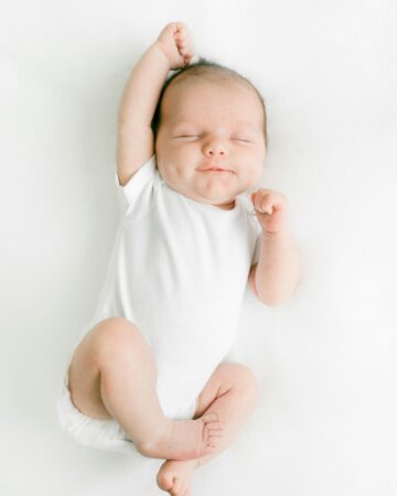 baby registry list. Image of newborn baby in white onesie stretching arm over head.