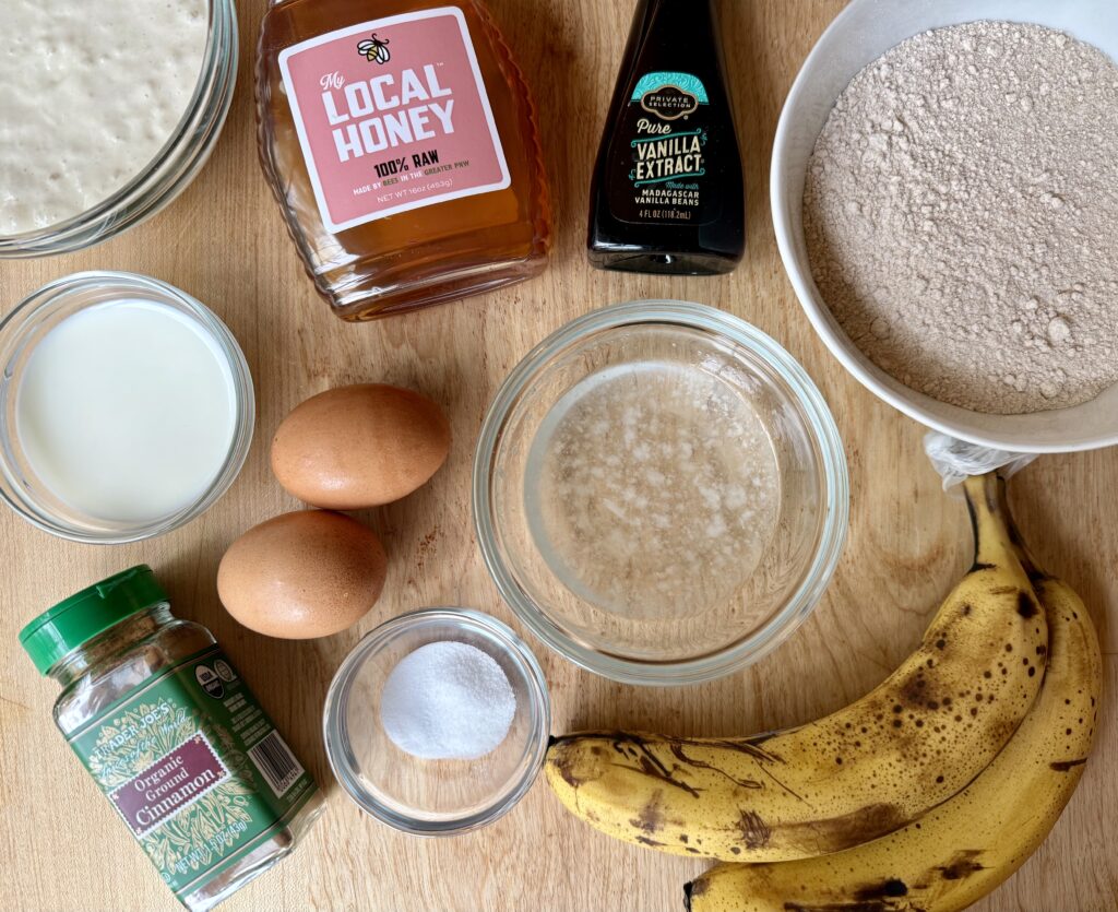 healthy banana bread recipe. image of ingredients for banana bread - sourdough starter, honey, vanilla, flour, milk, eggs, coconut oil, cinnamon, salt, and bananas.
