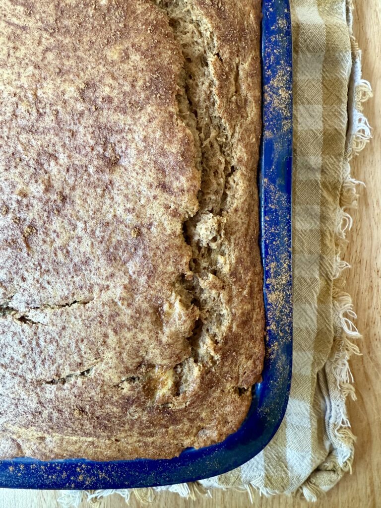 Close up image of loaf of banana bread in blue ceramic loaf pan on tan and white gingham napkin.